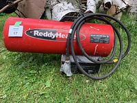 Red ReddyHeat construction heater on grass with attached cable and metal label showing BTU ratings.