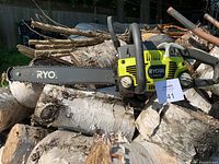 Ryobi chainsaw with bar and chain lying on wood logs outdoors