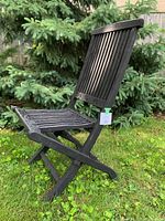 Side view of black teak patio folding chair on grass with a tag.