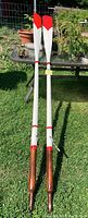 Photo of two wooden rowing oars with white blades tipped with red, resting on grass with oar locks attached.
