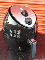 Front view of black and silver Faberware air fryer showing two control knobs and cooking icons for various foods.