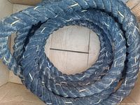 Coiled heavy duty rope with dark and lighter fibers seen in a cardboard box.