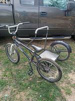 Black Impakt BMX bike with attached right-side carrier next to truck. Shows entire bike and carrier frame layout.