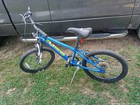 Side view of the blue and green Diamondback kids mountain bike leaning on a truck. Shows frame, tires, handlebars, seat, and pedal setup.
