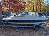 Side view of Bayliner boat on trailer showing white and green hull, windshield, and bow railing, with autumn leaves overhead
