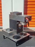 Side view of Bunn coffee maker showing three warming plates with removable lids, heating elements, and dispensing spout with red lever.