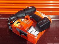 Black & Decker cordless drill with 7.2V battery attached, sitting on original box, angled view showing trigger and chuck.