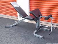 Side view of the adjustable weight bench showing padded seat and backrest with leg developer attachment and foam rollers.