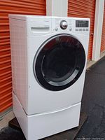 Front and side view of LG gas dryer showing closed glass door, control panel and pedestal drawer with some minor scuffs.