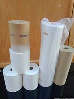 Six rolls of painting papers and masking materials placed against a wooden background. Rolls include white and brown papers, some wrapped and some labeled Easy Mask.