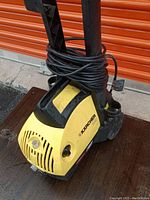 Pressure washer front view showing yellow casing, coiled power cord, and venting details