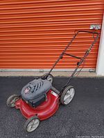 Side view of the red Yard Machines push lawn mower showing front and rear wheels, handle, and motor top.