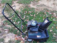 Front angle showing the Craftsman 5 HP snow blower on grass with some fallen leaves, highlighting the engine and snow chute.