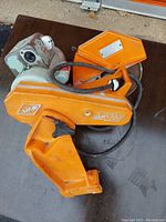 Orange Mk101 tile cutter resting on a brown surface, showing main body and cables.