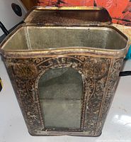 Open antique tin canister with ornate decorative detail and arched window