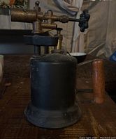 Front view of antique welding torch showing black metal and wooden handle with brass valve top