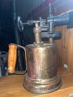 Side view of antique brass blowtorch showing wooden handle and brass body with knob valve.