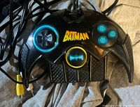 Front view of black Batman-shaped game controller with blue buttons and yellow Batman logo