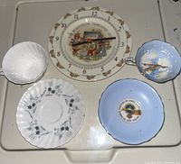 Photo showing the Bunnykins clock plate with clear clock hands, a white teacup with blue floral pattern and matching saucer, and a blue teacup with floral design and its saucer.