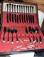 Full cutlery set with knives, forks, spoons, and small decorative forks arranged in red fabric-lined case
