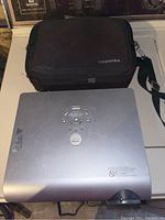 Silver Toshiba projector on table with Toshiba branded soft carrying case behind it.