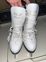 Front view of the white CCM Competitor figure skates showing gold lettering on tongues and white laces.