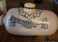 Photo showing front view of cream ceramic foot warmer with black printed text and decorative designs.