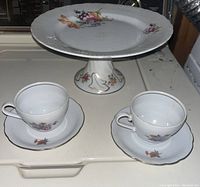 Porcelain cake platter with pedestal, two teacups, and saucers featuring floral designs