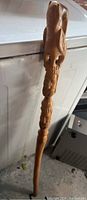 Full view of carved wood walking stick showing detailed carved figure near the top and other carvings along the shaft.