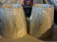Front view of two off white plastic lampshades showing gathered fabric design with glossy finish.