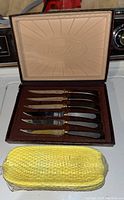 Six stainless steel steak knives with dark wooden handles arranged inside a brown velvet box embossed with the Glo-Hill brand.