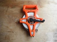 Front view of the orange plastic casing measuring tape showing Benchmark branding, handle, and manual crank.