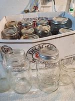 Two boxes of Mason jars in a Dragon beer cardboard box; jars vary in size and have metal lids, some open jars are visible in front