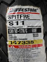 Photo of tire label showing Bridgestone Spitfire S11 branding, size 130/90-17, bias tubeless type, and warning label.