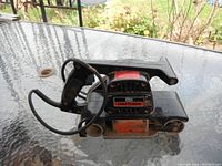 Craftsmen black metal belt sander on glass table showing front view with sanding belt and power cord