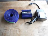 Three items including Nextech power inverter, blue strapping roll, and black mechanical timer switch on wood surface