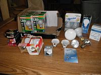 Lot of 22 assorted new light bulbs including LED, halogen, flood, and incandescent types arranged on table with boxes and packaging visible.