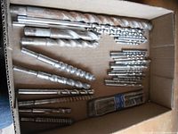 Top view of the masonry drill bits in a cardboard box showing various sizes including large, medium and small diameters, and a small sealed pack of new bits.