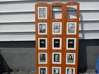 Front view of wooden three-panel room divider with black and white photos in picture frames.