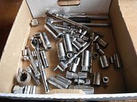 Top view of cardboard box filled with assorted metal sockets and ratchets showing variety in sizes and styles.
