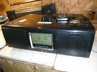 Front view of teak radio model SR-L200I showing digital clock display, speakers, and iPod dock on top
