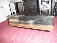 Wide shot of Technics SL-235 turntable with dust cover on, showing wood grain base and dark plastic dust cover.