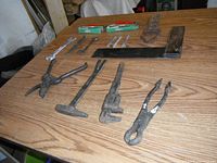 Full view of mixed vintage tools including wrenches, pliers, hammer, green utility knives, metal square, and other hand tools arranged on a wooden surface.