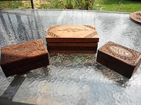 Full view of three wooden boxes showing top designs and stacked arrangement on glass table outdoors