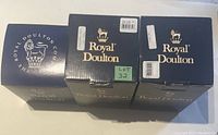 Three original Royal Doulton boxes in navy blue with gold logos and text, each labeled and marked for the respective figurine model and lot number.