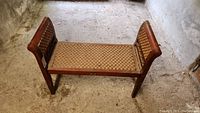 Full view of the indoor wooden bench with woven seat and arms, showing overall structure and condition.