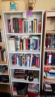 Front view of solid white bookcase filled with many books and a few smaller objects on bottom shelf and top