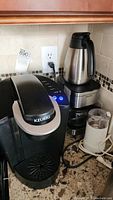 Keurig coffee maker, Krups coffee maker with insulated carafe and Mr. Coffee grinder on kitchen counter