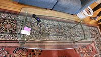 Coffee table with two clear glass tops and brass base sitting on decorative patterned rug near blue sofa.