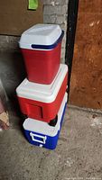 Stack of three coolers: red Coleman cooler on top, red Igloo cooler in the middle, blue Rubbermaid cooler on the bottom